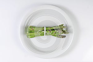 Bunch of asparagus tied with twine on white plate