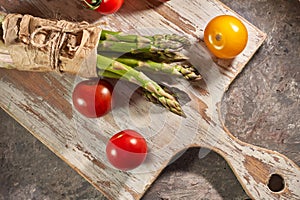 Bunch of asparagus and tomatoes on wooden cutting board