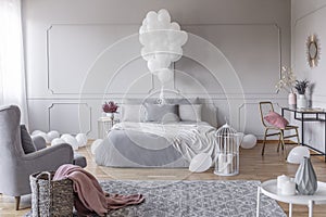 Bunch of balloons above king size bed with grey pillows and duvet in elegant bedroom with golden chair with pink pillow and