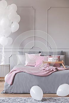 Bunch of balloons in elegant grey bedroom interior with king size bed with grey bedding and pink pillows and blanket