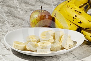 A bunch of bananas, a sliced banana, and an apple on a plate on a table. Selective focus