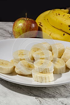 A bunch of bananas, a sliced banana, and an apple on a plate on a table. Selective focus