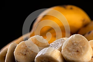 A bunch of bananas and a sliced banana in a bowl on a table