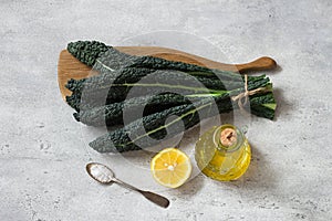 Bunch of black tuscan kale (cavolo nero or lachinato kale), olive oil, lemon and salt on a gray textured