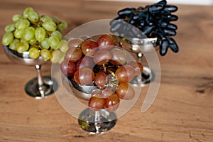 A bunch of blue, green and red grapes in metal bowls on a wooden table. Food, healthy eating. Soft selective focus