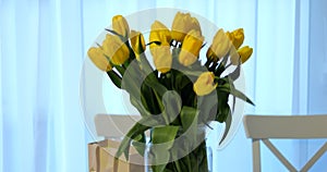 Bunch bright intense yellow tulips vase with gift bag light background. Spring