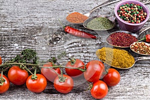 Bunch of cherry tomatoes, herbs, small bowl and antic metal spoons with different kinds of spices, sea salt and red hot chili pep