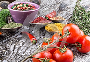 Bunch of cherry tomatoes, herbs, small bowl and antic metal spoons with different kinds of spices, sea salt and red hot chili pep