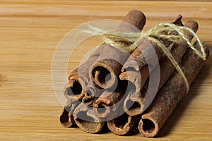 Bunch of cinnamon sticks tied with wooden thread on the wooden background.