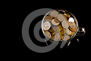 Bunch of coins in a glass cup over black background