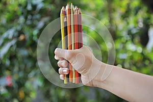 Bunch of colored pencil in hands. Blurry green garden background. Copy space.