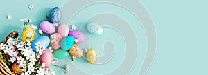 Bunch of colorful eggs in a basket with spring flowers on a blue Easter background