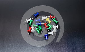 A bunch of colorful paper push pins or thumbtacks on bright dark rough background