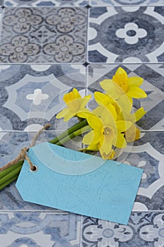 Bunch of daffodils narcissus tied with string with a blank blue tag on a tiled surface.  Spring Saint Davidâ€™s Day concept