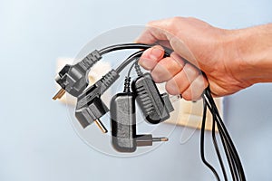 A bunch of disconnected electrical plugs with cables in a hand in room