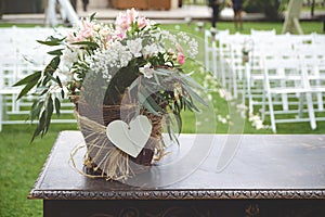 Bunch of flowers on a wooden desk against the white chairs aisle in a wedding celebration.