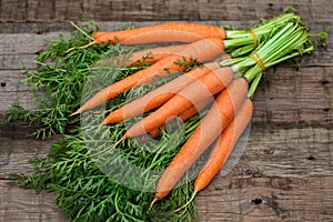 Bunch of fresh carrots with green leaves over wooden background