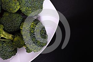 Bunch of fresh green broccoli on white plate over black wooden background. Healthy food. Diet food