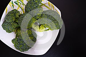 Bunch of fresh green broccoli on white plate over black wooden background. Healthy food. Diet food