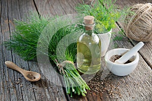 Bunch of fresh green dill, mortar of fennel seeds and dill oil.