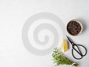 A bunch of fresh green garden thyme, slice of lemon, black scissors and black pepper in bowl on a light background. Top view. Copy