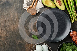 Bunch of fresh green organic asparagus spinach, avocado, chicken eggs, pepper seasoning and an empty plate in middle on black old