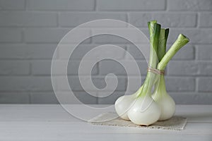 Bunch of fresh green spring onions on white wooden table against brick wall, space for text