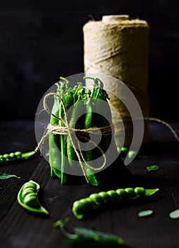 Bunch of fresh mature pods of green peas tied with a rope on black wooden background. Bio healthy food. Green peas, pods.