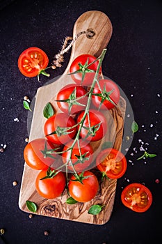 A bunch of fresh organic cherry tomatoes with sea salt and basil in olive cutting board