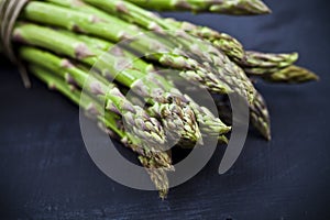 Bunch of fresh raw garden asparagus closeup on black board background. Green spring vegetables