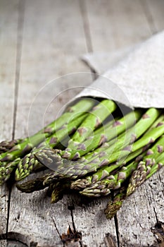 Bunch of fresh raw garden asparagus closeup and linen napkin on rustic wooden table background