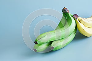 Bunch of fresh ripe green plantain compared to regular yellow bananas against a blue background. Copy space