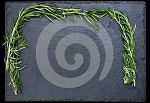 Bunch of fresh rosemary on a black slate, stone or concrete background.