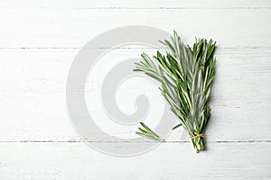 Bunch of fresh rosemary on white wooden table, top view with space for