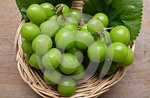 Bunch of fresh Sweet Green Shine Muscat (Vitis vinifera) grape and leaf in Bamboo basket on wooden table in garden .