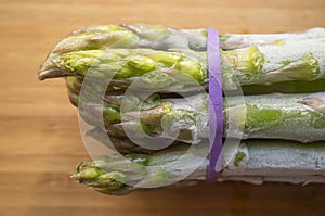 Bunch of frozen wild asparagus tied with rubber tape from ecological agricuture over wooden background photo