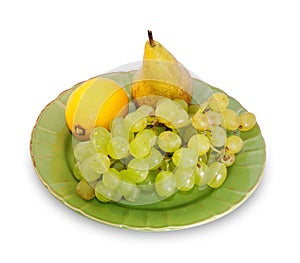 Bunch of grapes, lemon and pear on green plate isolated