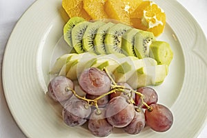 Bunch of grapes, sliced kiwi, apple and orange fruits in white plate