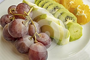 Bunch of grapes, sliced kiwi, apple and orange fruits in white plate