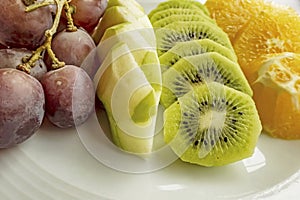 Bunch of grapes, sliced kiwi, apple and orange fruits in white plate