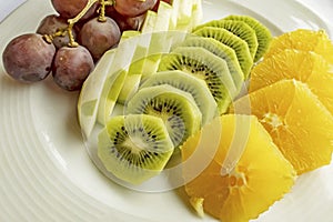 Bunch of grapes, sliced kiwi, apple and orange fruits in white plate