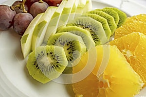 Bunch of grapes, sliced kiwi, apple and orange fruits in white plate