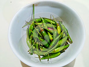 a bunch of green chilies in a bowl on a white background