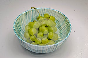 Bunch of green grapes inside a white bowl with blue stripes