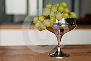 A bunch of green ripe grapes in a metal bowl on a wooden table. Food, healthy eating. Soft selective focus