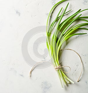 A bunch of green spring onions tied with a rope on a light stone background.