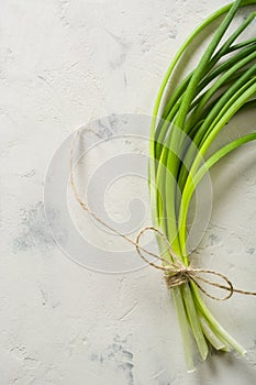 A bunch of green spring onions tied with a rope on a light stone background.