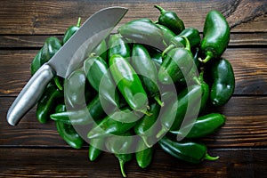 Bunch of JalapeÃ±o peppers on a kitchen counter waiting to be sliced up with a knife by the chef.