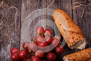 A bunch of juicy large red grapes and fresh crispy wheaten baguette on a table of dark old wooden boards