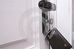 A bunch of keys with a leather key case inserted in a keyhole in order to open or lock a white wooden door, home security and